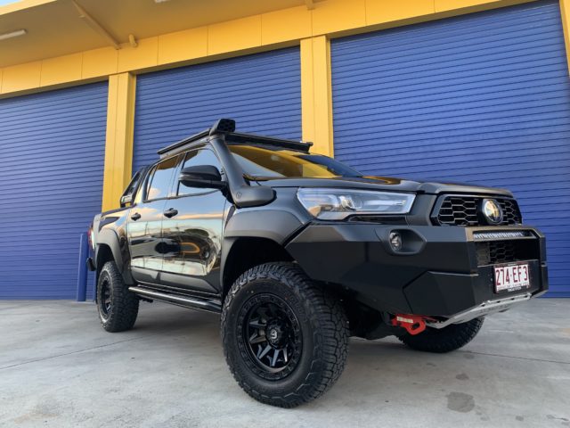 A black Toyota Hilux parked in front of a garage, transformed from 'Everyday' to 'Out-of-this-World'.