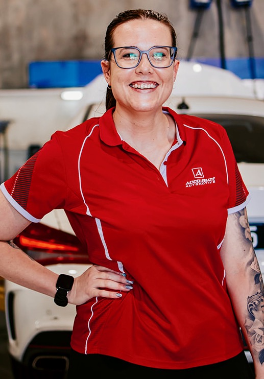 Carl Millward, wearing glasses and a red polo shirt, stands in front of a white car, smiling with one hand on his hip.