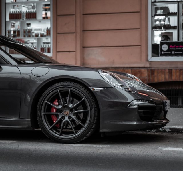 A silver Porsche parked on the side of a street in need of servicing.