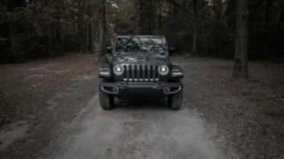 A black jeep parked on a dirt road in the woods.